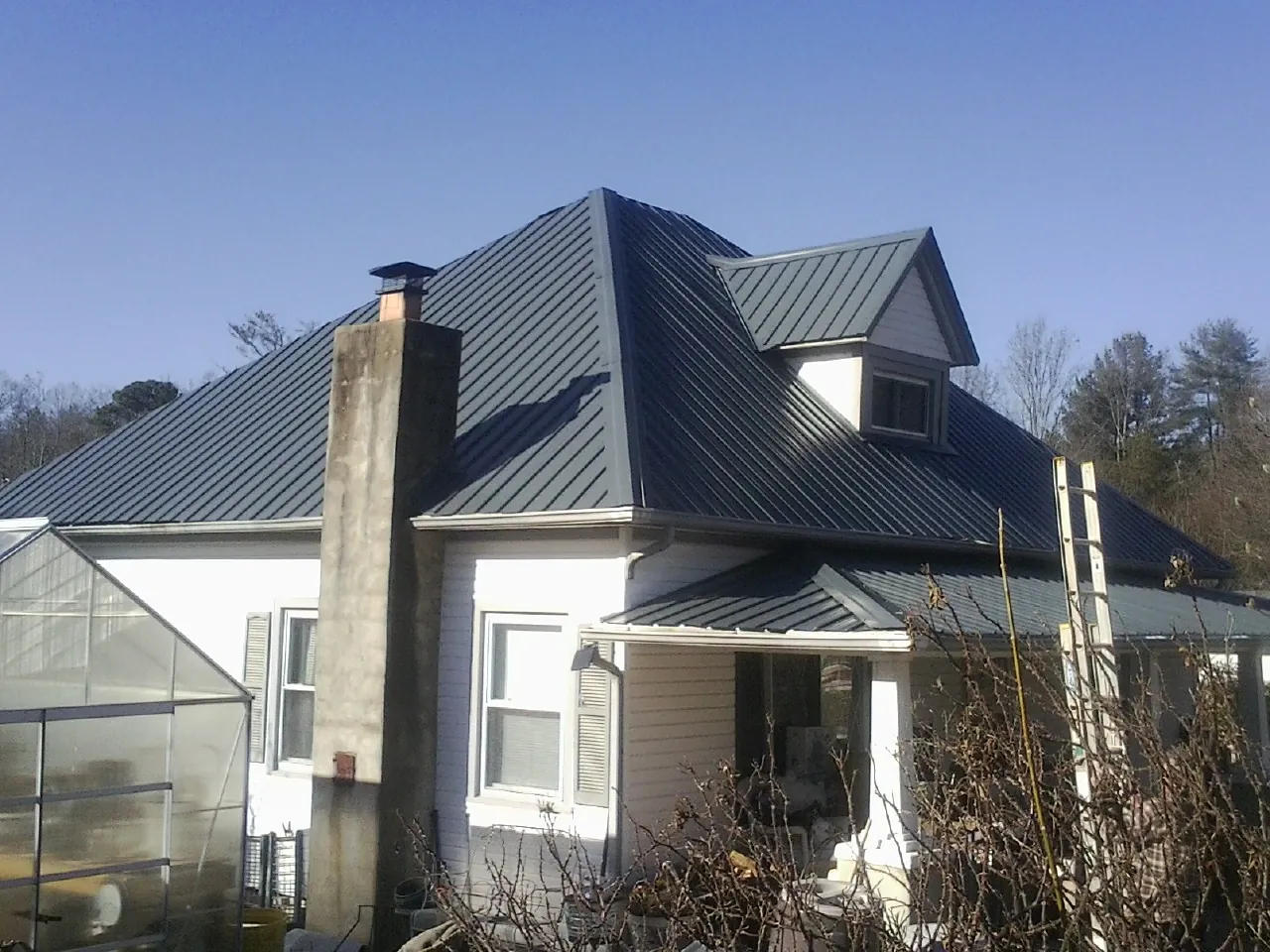 Dark blue standing seam metal roof on a white farmhouse with dormer — Slate & Tile Roof Repair by Roofing Brothers in Manchaca