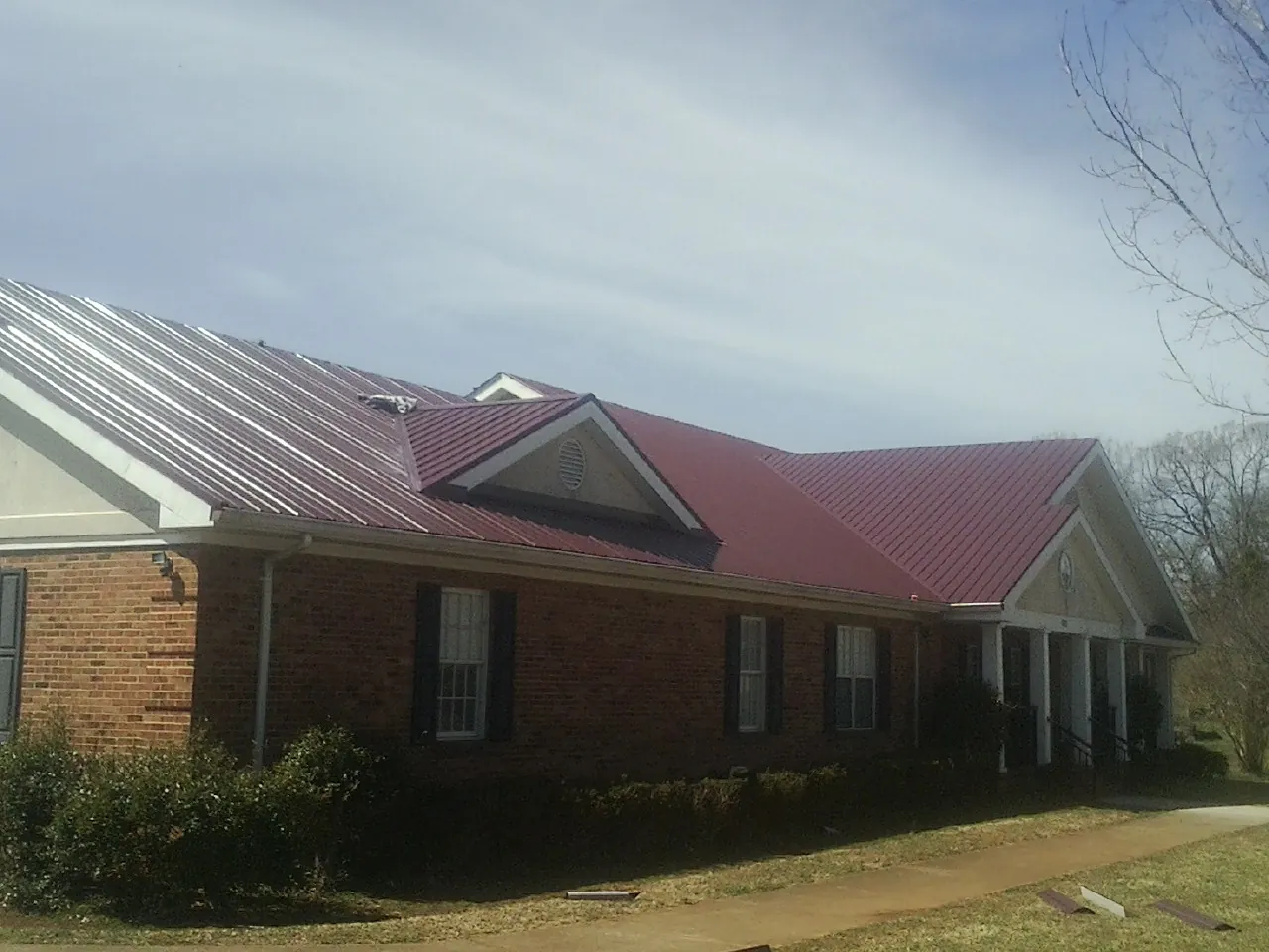 Red metal roof with gabled entries on a long brick building, from a Hail Damage Roof Repair job in Manchaca