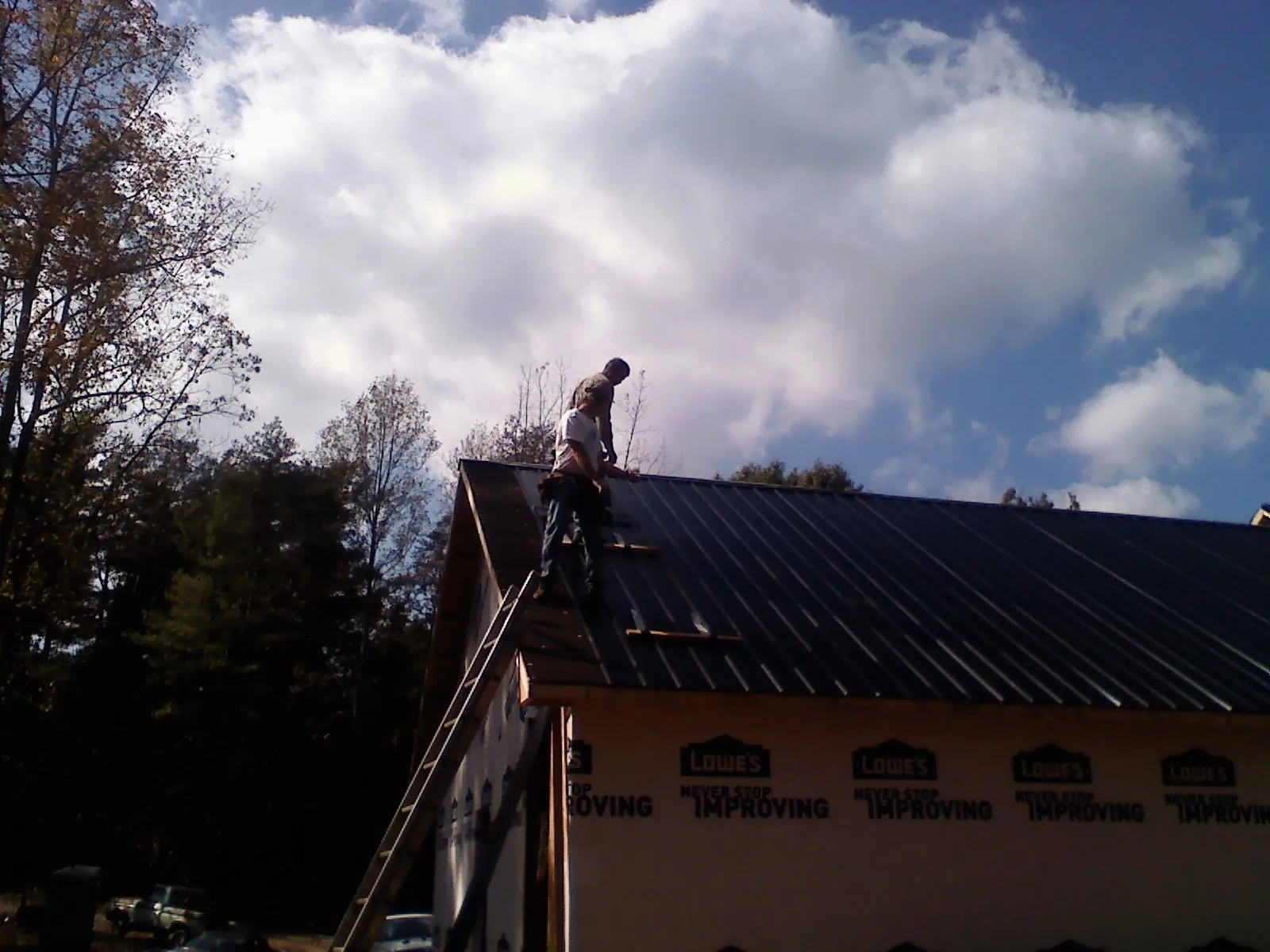 Roofer fastening dark metal panels high against a cloudy sky, from a Roof Inspection job in Manchaca