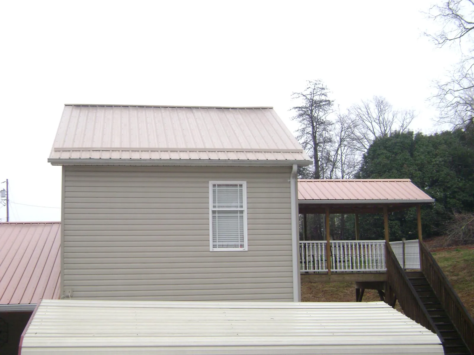 Tan metal roofs on a two story addition and attached porch, from a Roof Replacement job in Manchaca